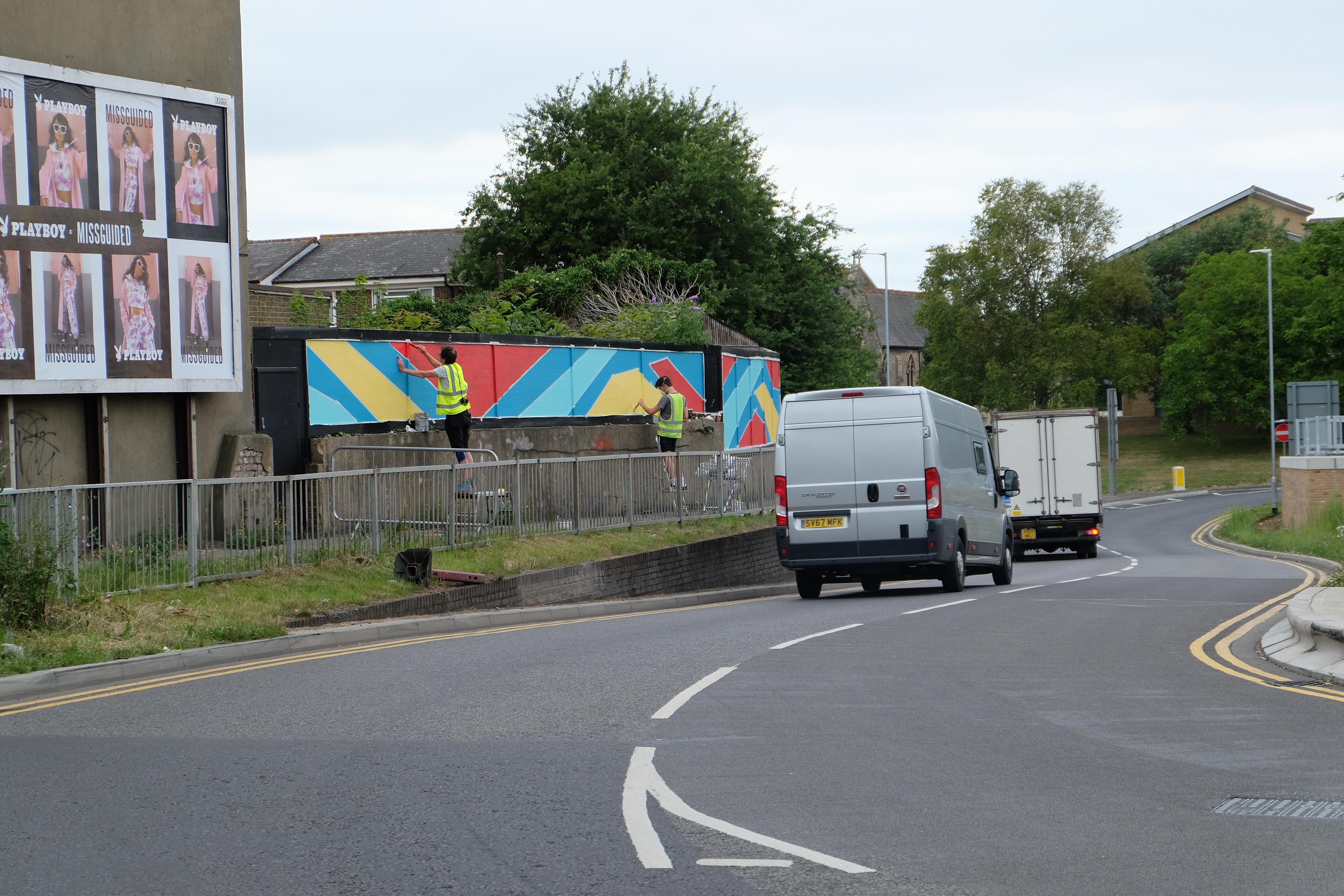 Artists hand-painting the outdoor mural installation in Sittingbourne on hoarding boards