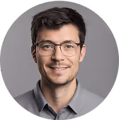 A person wearing glasses and a gray shirt smiles at the camera.