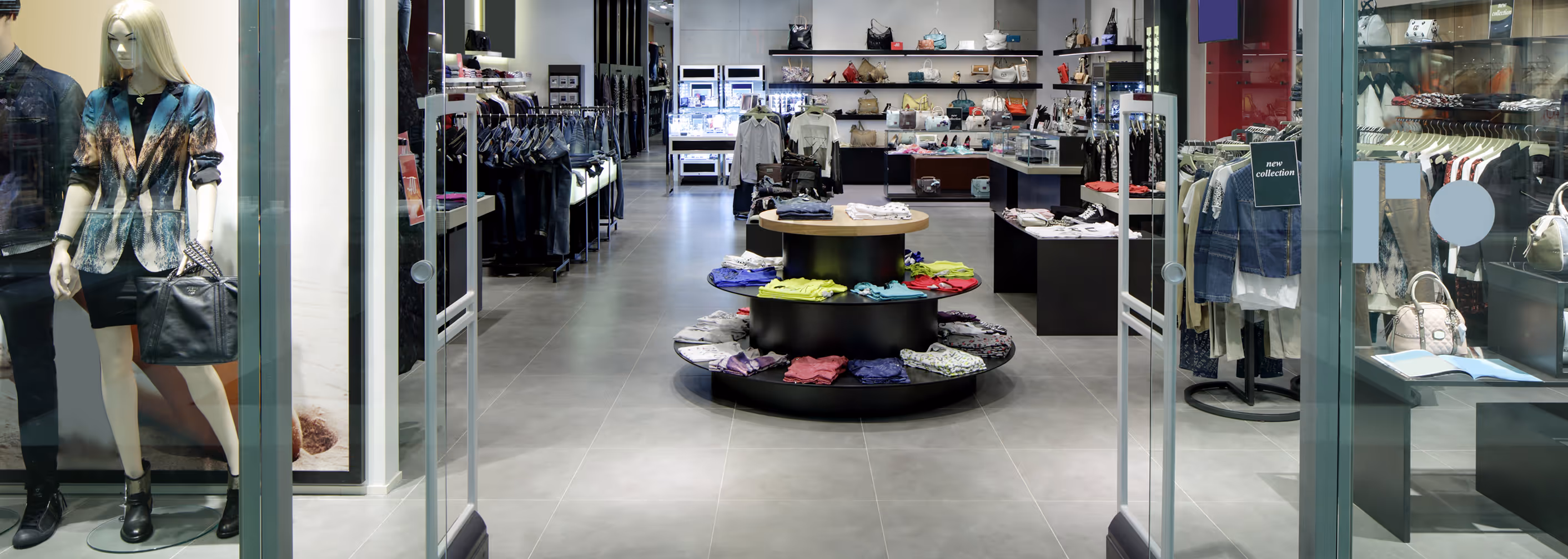 Clothing store interior with neatly arranged garments on racks and folded items on a round display table.