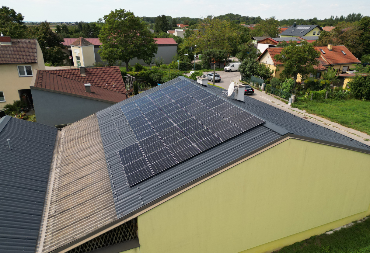 Solar panels installed on a sloped metal roof of a yellow building in a suburban neighborhood.