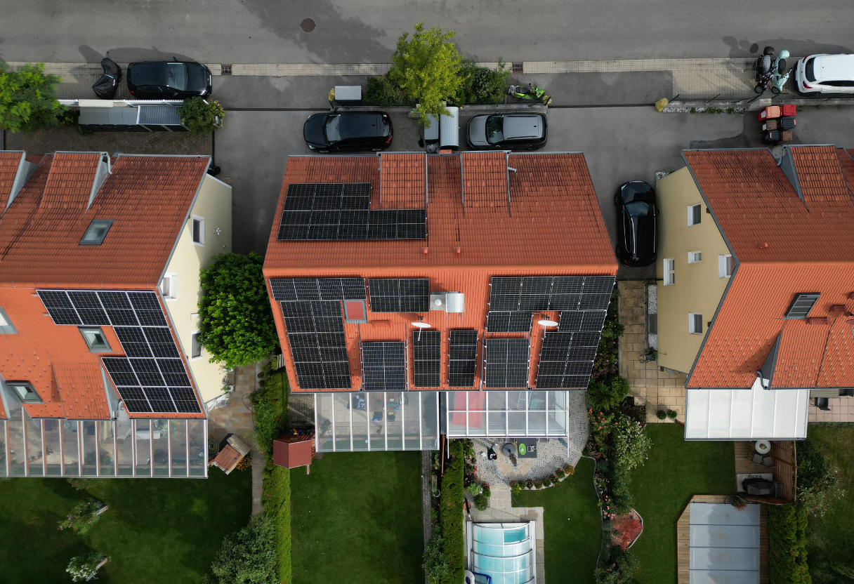 Aerial view of three houses with red tiled roofs, two of which have solar panels installed, and neatly maintained green yards.