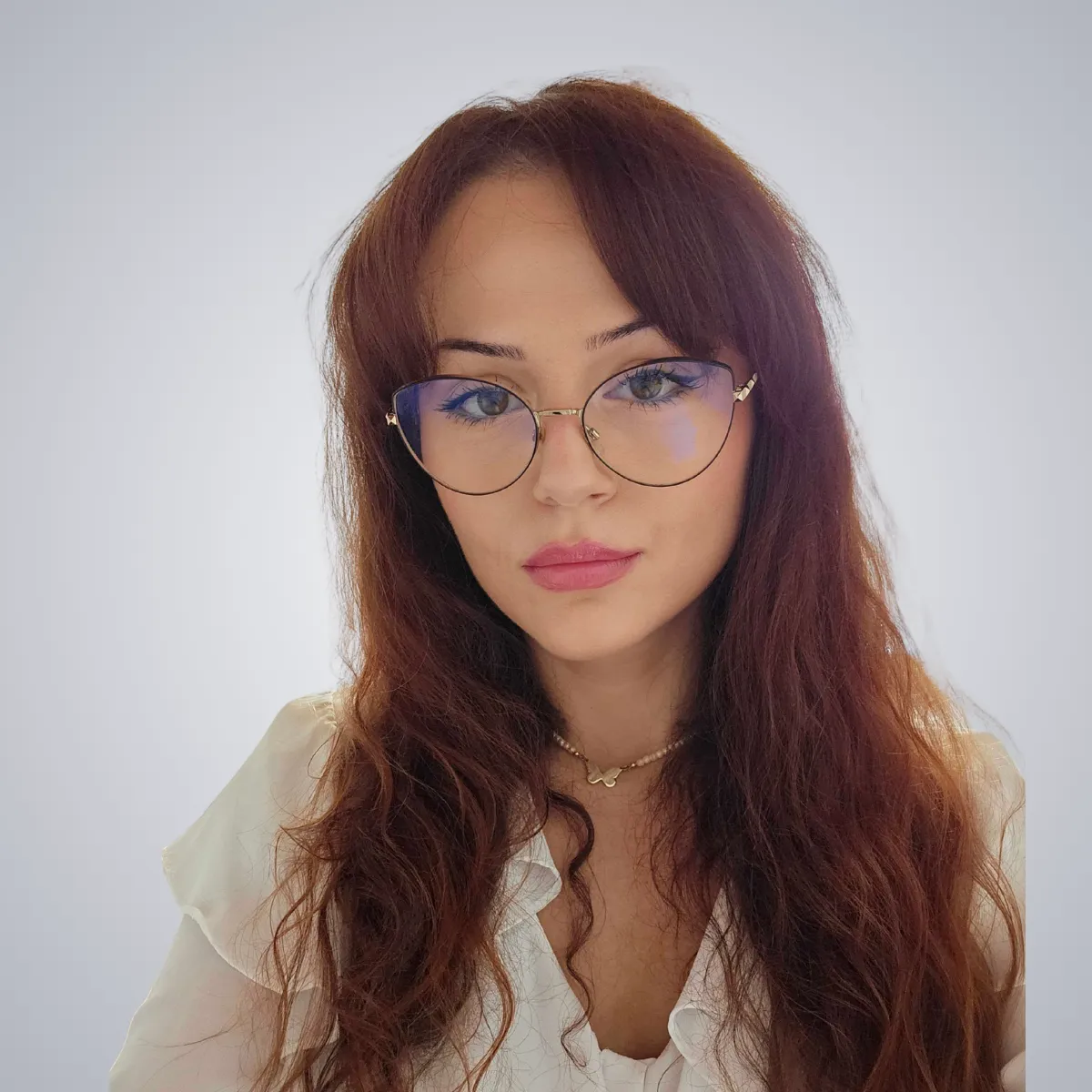 Woman with long wavy brown hair wearing round glasses and a white blouse.
