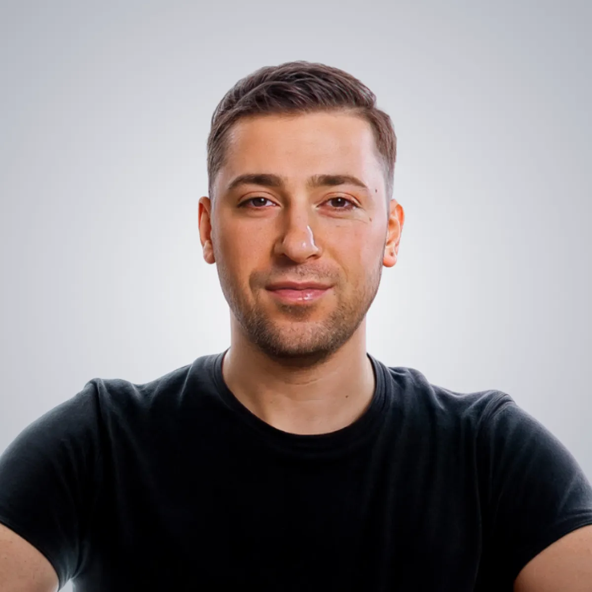 Portrait of a young man with short brown hair wearing a black t-shirt against a plain light background.