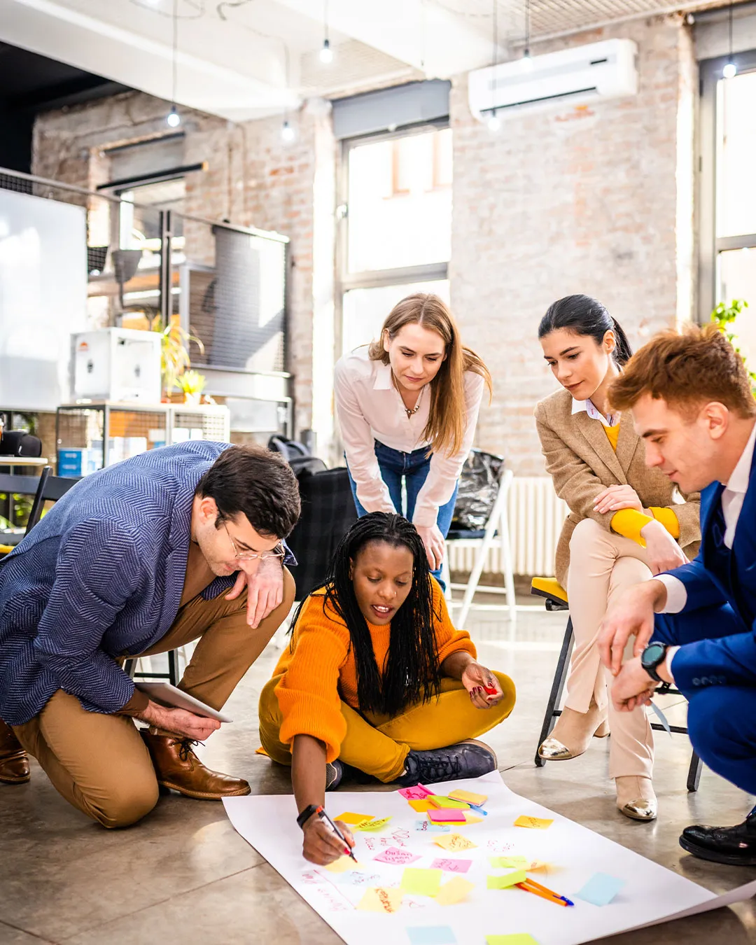 Gruppo di cinque colleghi che collaborano su un grande foglio con post-it colorati in un ufficio moderno.