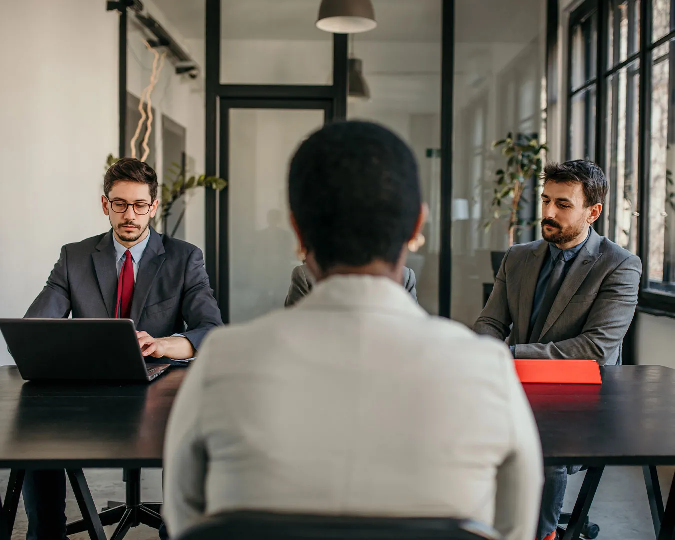Due uomini d'affari in abito formale che fanno un colloquio di lavoro con una donna vista di spalle.