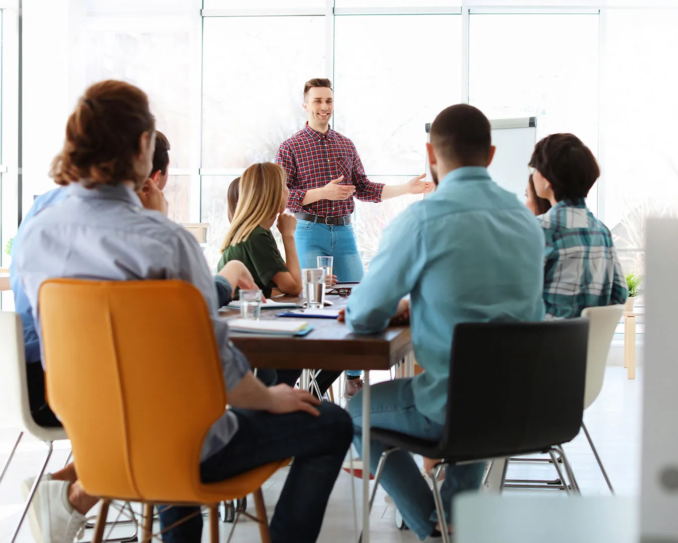 Uomo che parla in piedi davanti a un gruppo seduto intorno a un tavolo in una sala riunioni luminosa.