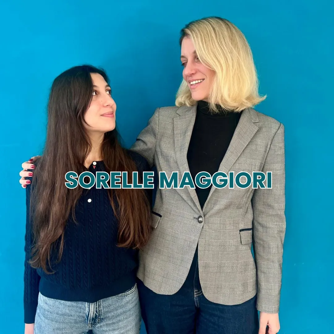 Due sorelle si guardano sorridenti con un braccio sulle spalle dell'altra, davanti a uno sfondo blu e la scritta Sorelle Maggiori.