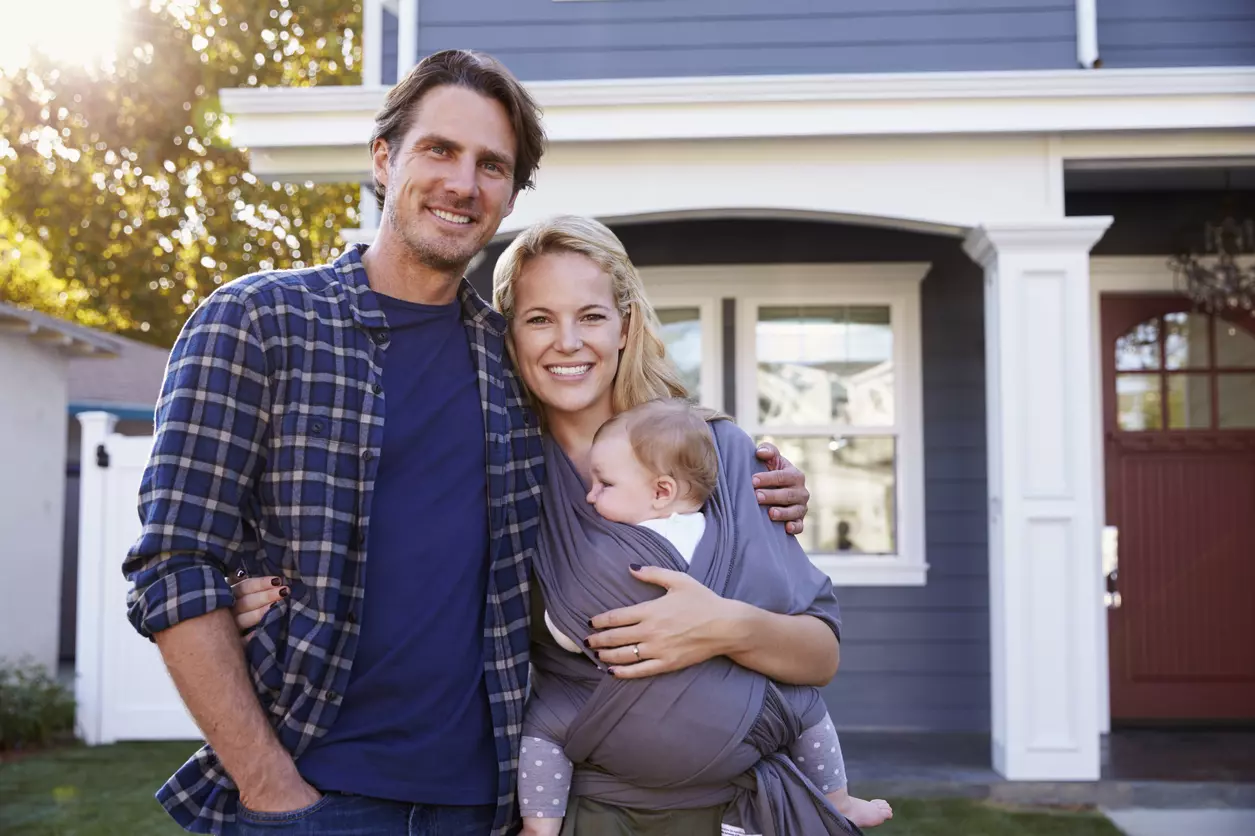 `Happy couple with baby outside house`