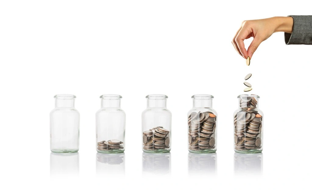 `Hand putting money into a jar of coins`