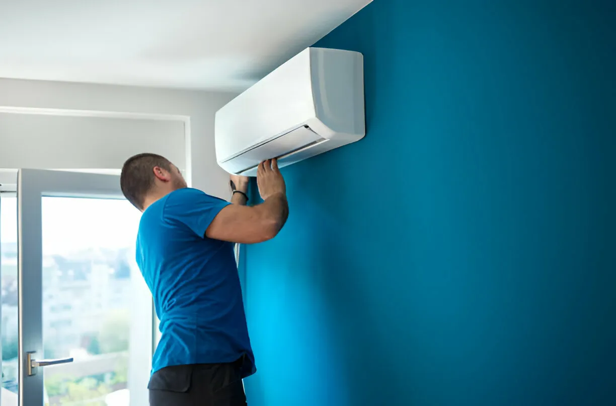 "Technician installing a mini-split AC unit on a blue wall"