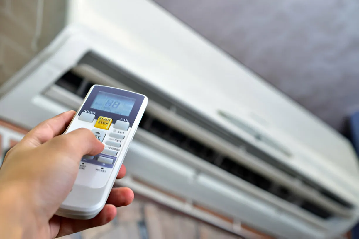 Hand holding remote, pointing at AC unit.