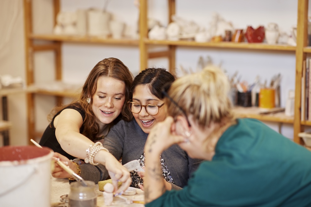 Tre unga kvinnor skapar keramik tillsammans vid ett bord i en verkstad.