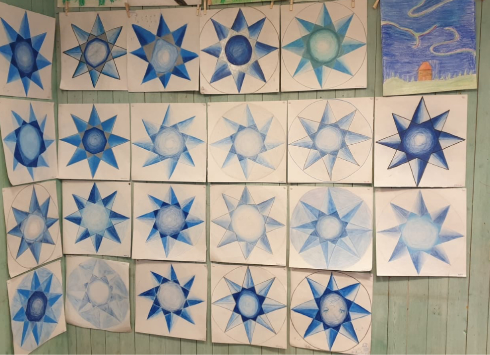 Vägg med flera teckningar av blå stjärnor i olika nyanser och mönster, arrangerade i rader på vitt papper.