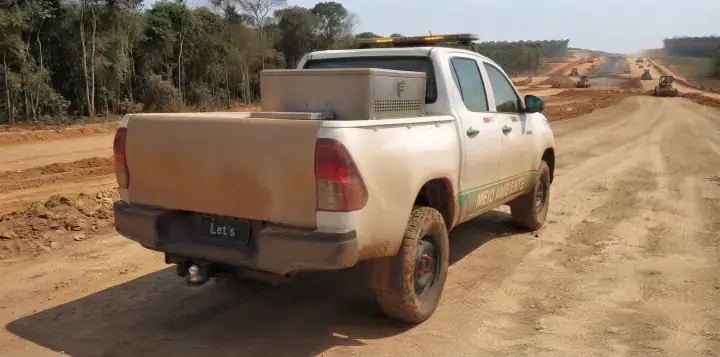 Picape vista de trás com engate de reboque de bola cromada sob o para-choque, em estrada de acesso a obra