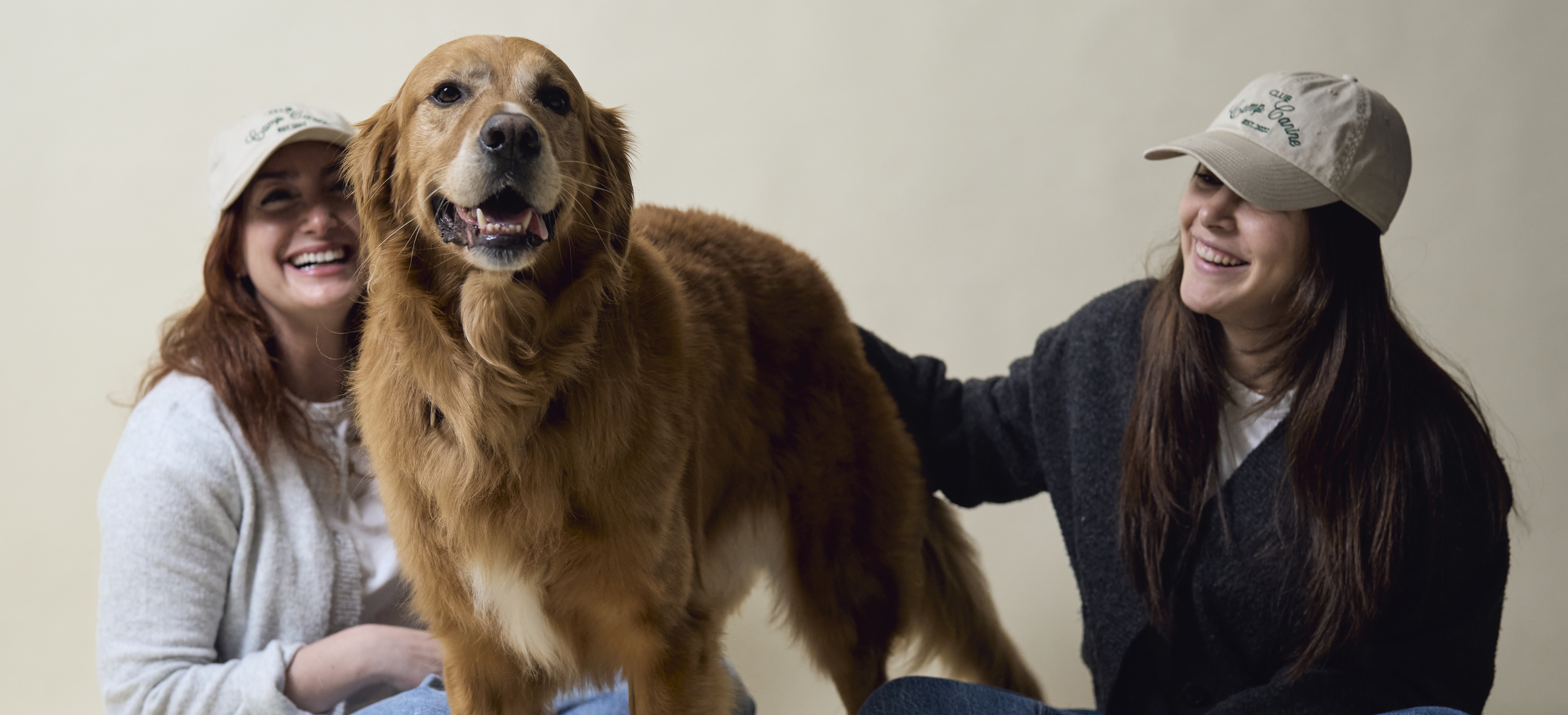 Two woman sitting on the ground petting a golden retriever