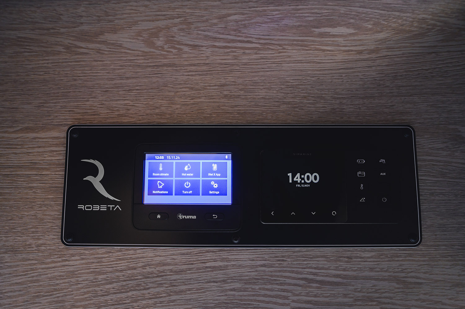 Robeta control panel mounted on wood surface showing Truma system screen with options for room climate, hot water, notifications, and settings alongside a digital clock display.