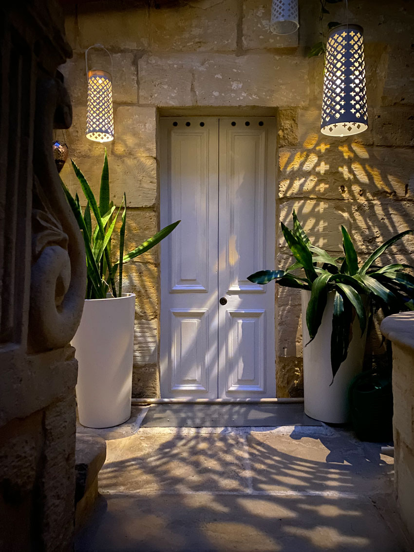 Door to library in courtyard at night lit by hanging lamps. Malta house for sale.