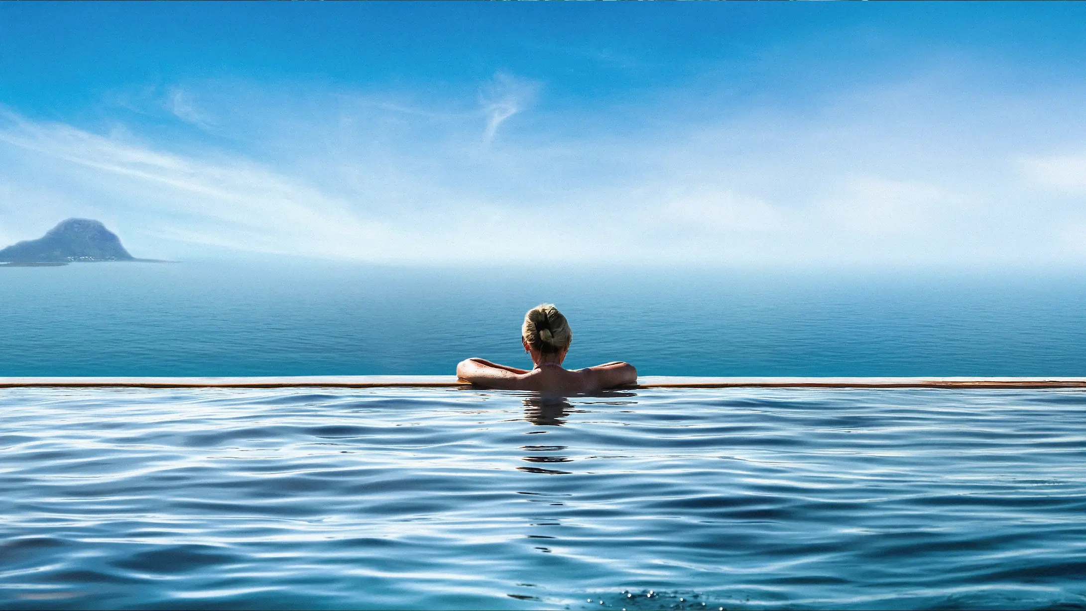 Une femme se baignant dans une piscine à débordement avec une vue panoramique sur le Morne à l'ile maurice