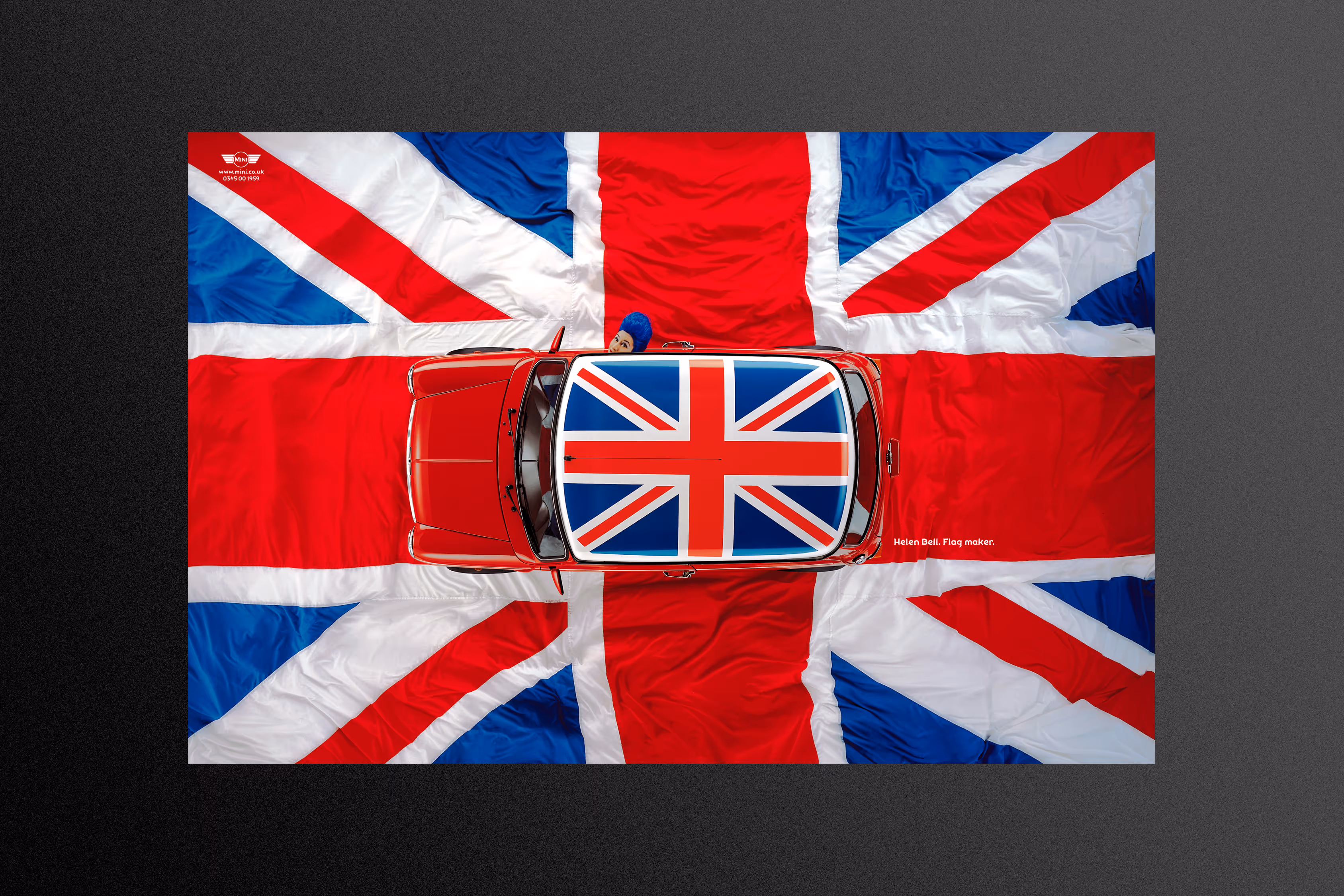 Overhead shot of a Mini Cooper with a union jack flack on its roof. The background is a real life, much larger version of the the flag.