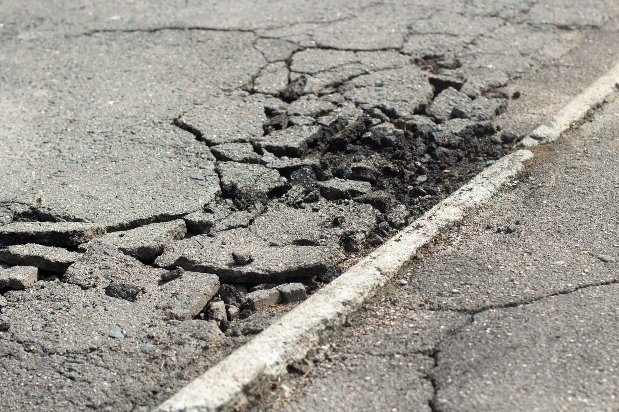Badly cracked and broken asphalt road surface