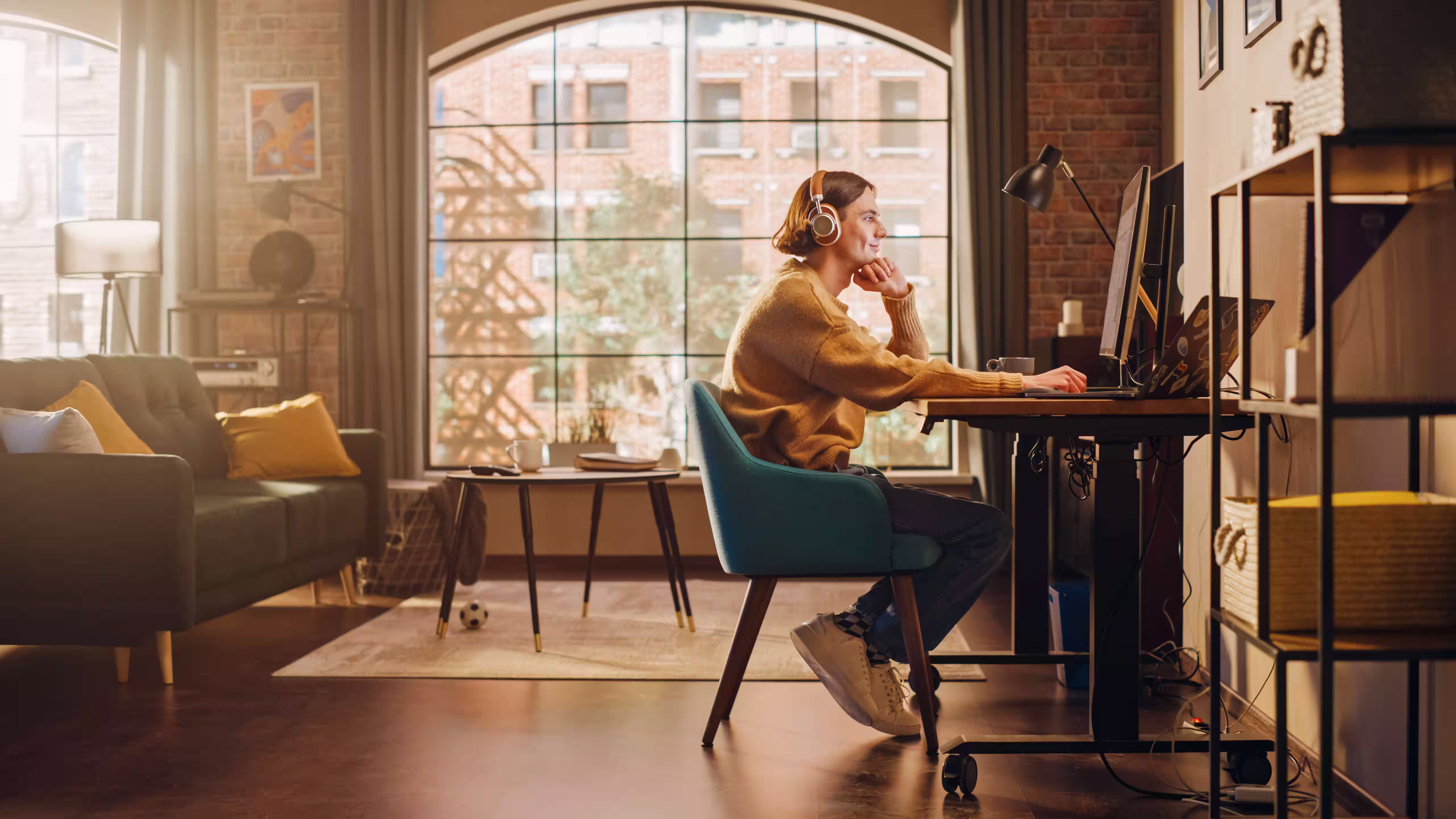 Person wearing headphones working at a desk beside a sunlit window.