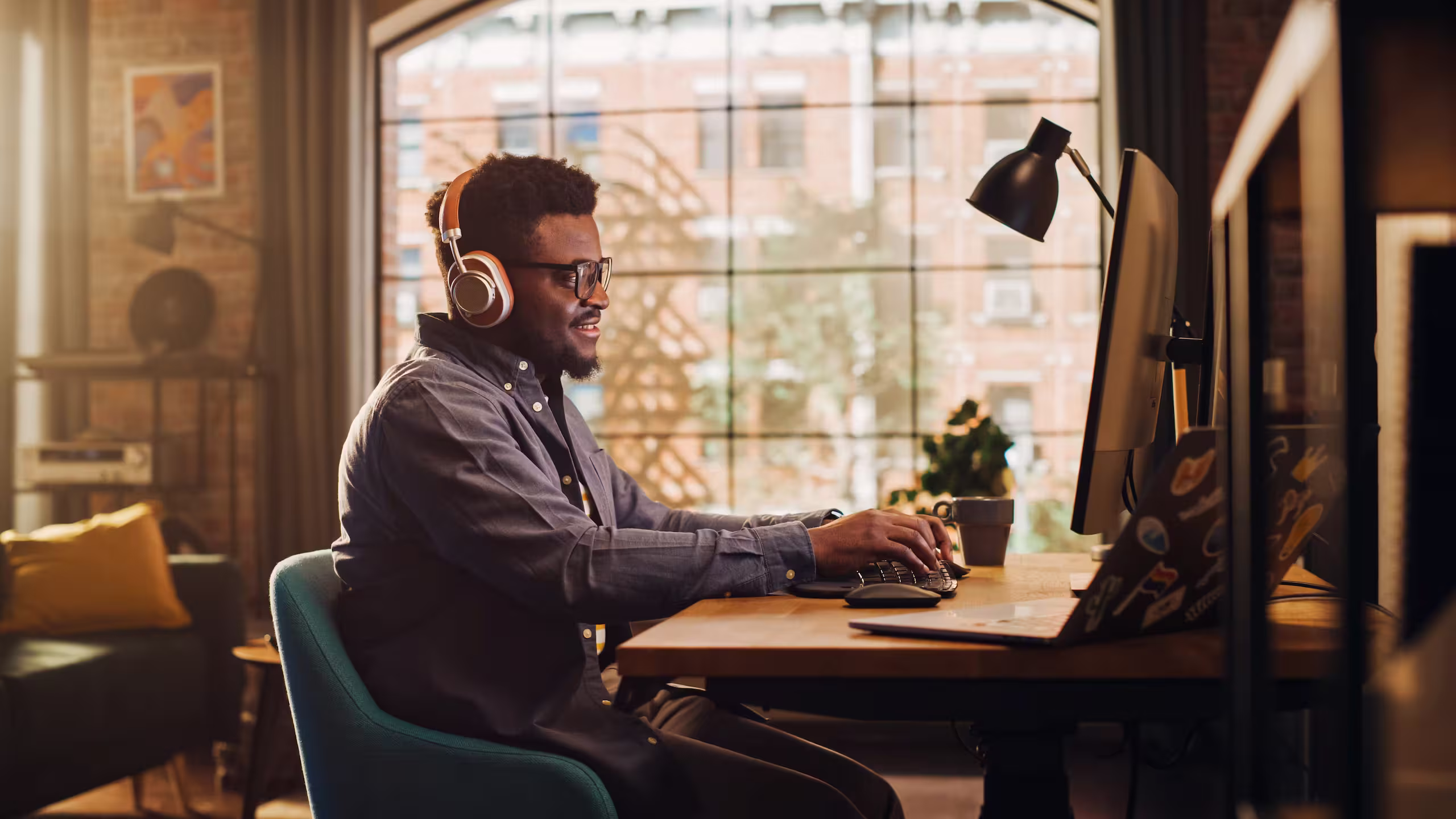 Man wearing headphones working at a desktop computer beside a window.