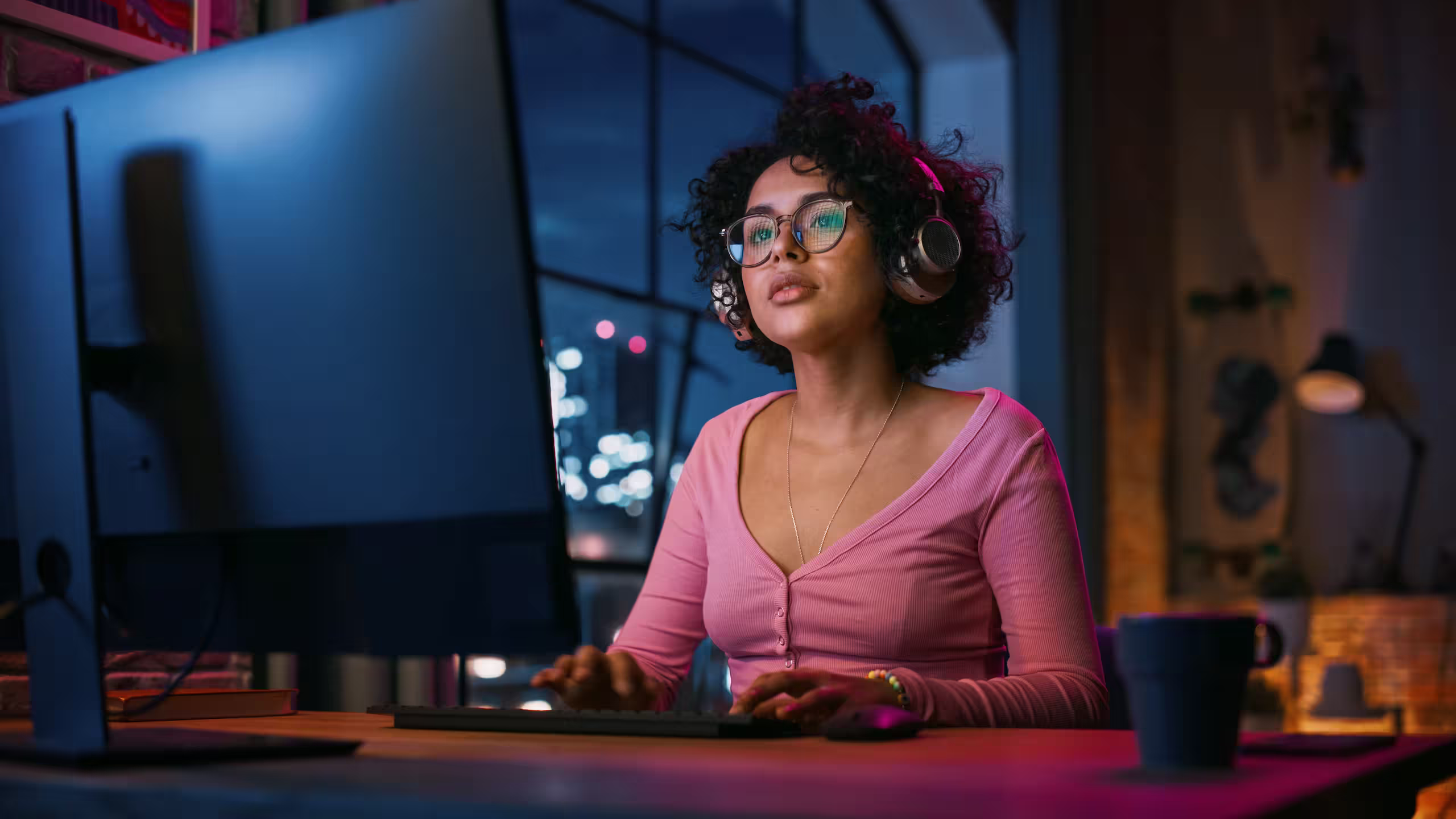Woman wearing glasses and headphones working at a desktop computer.