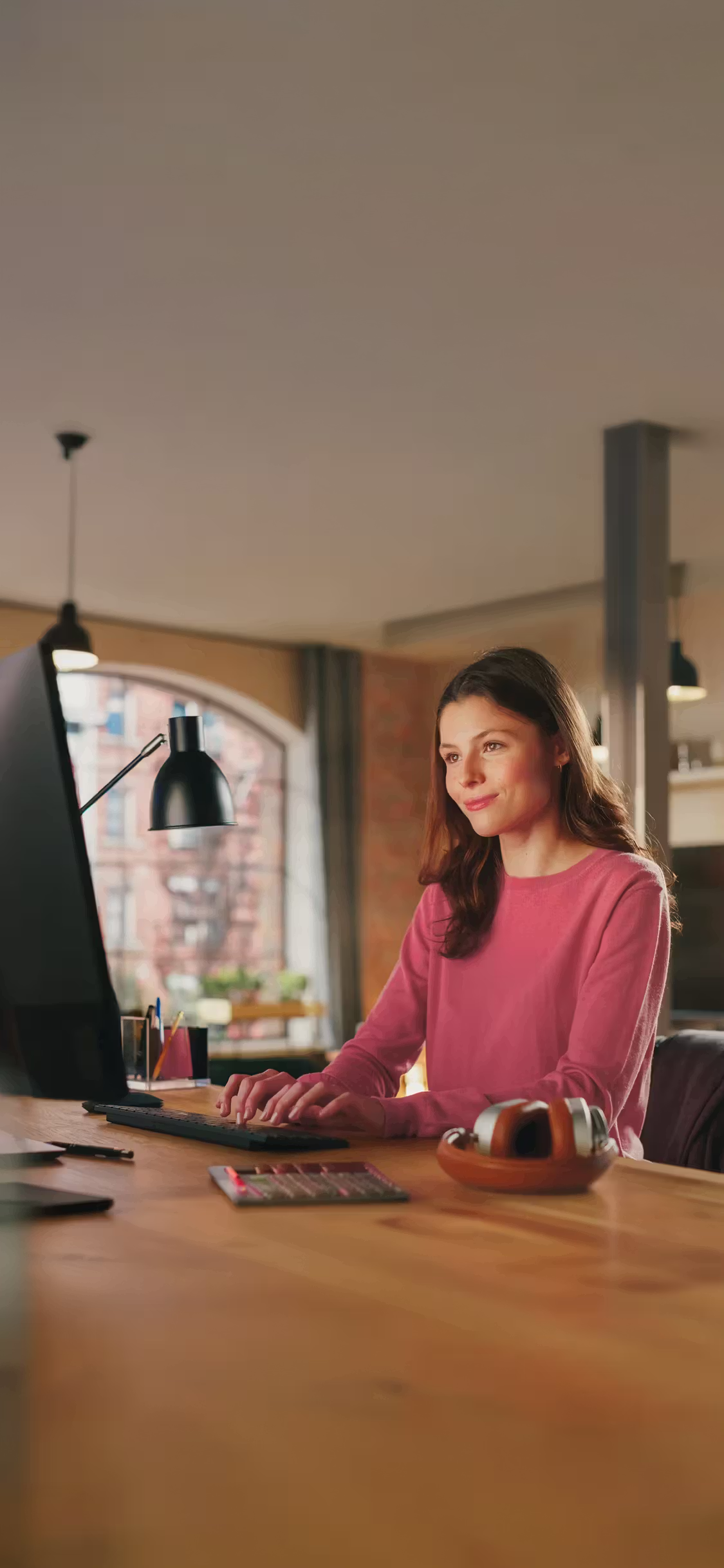 Woman working at a desktop computer at a wooden table.