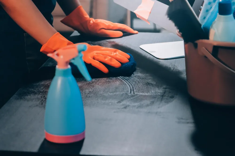 Reinigungskraft wischt Tischoberfläche mit Reinigungsmittel und Handschuhen für hygienische Sauberkeit.