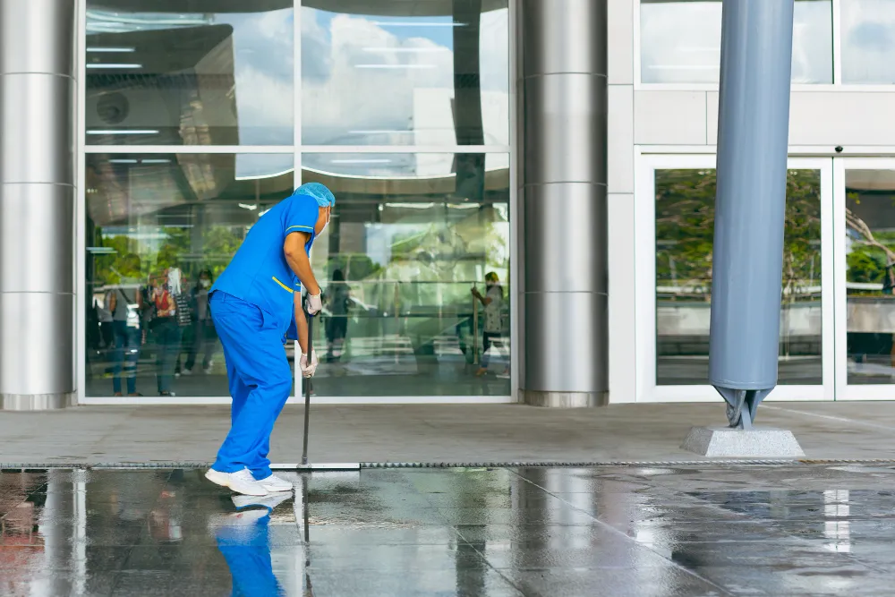 Reinigungskraft in blauer Uniform wischt Boden vor moderner Glasfassade