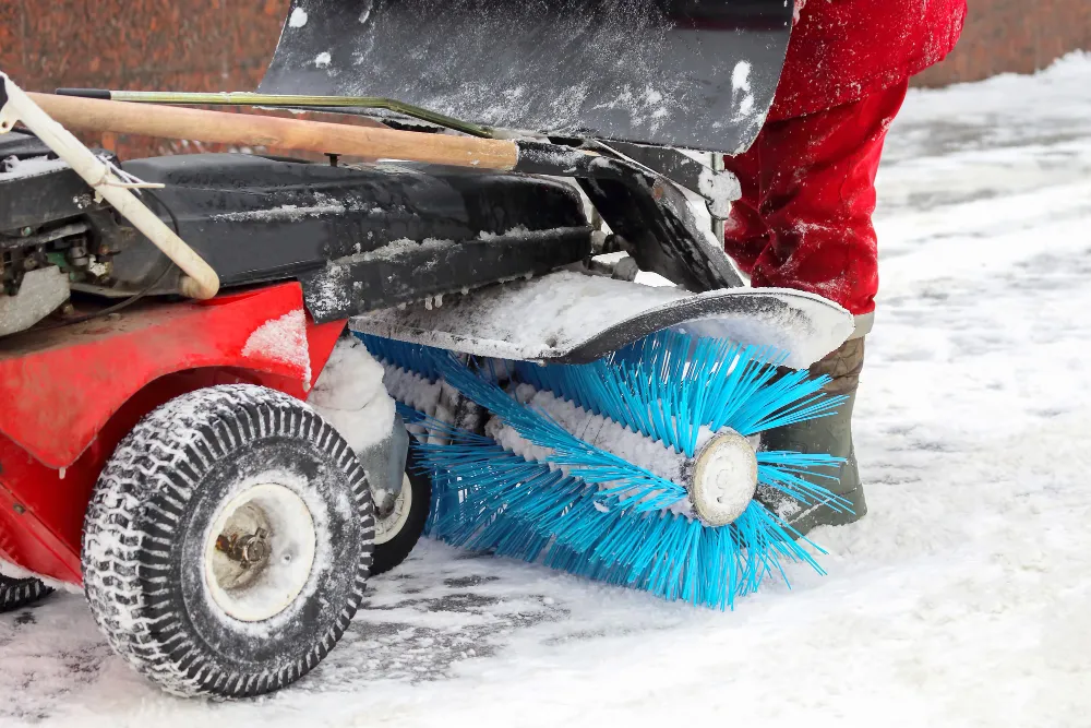 Schneefräse mit blauer Bürste räumt Schnee auf verschneitem Boden