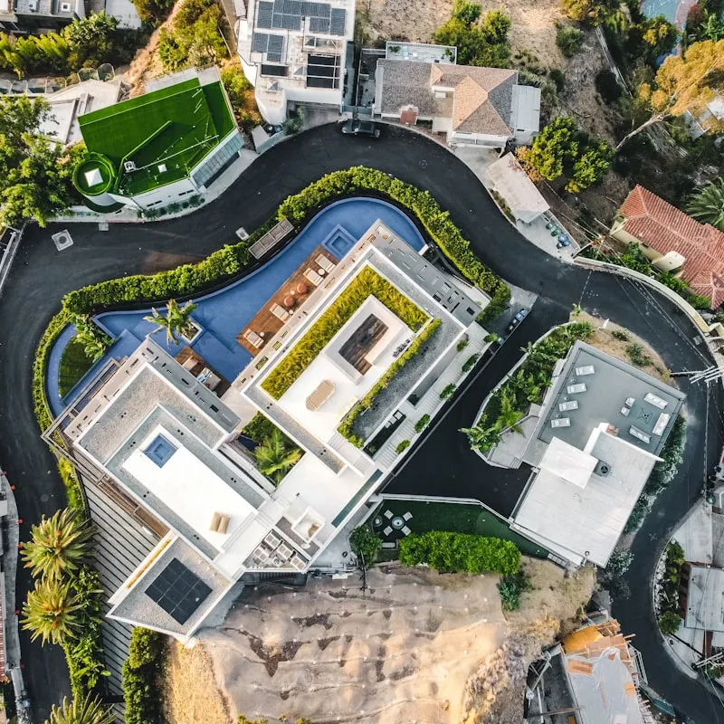 Aerial view of a modern residential property with multiple buildings, landscaped greenery, curved roads, and solar panels on rooftops.