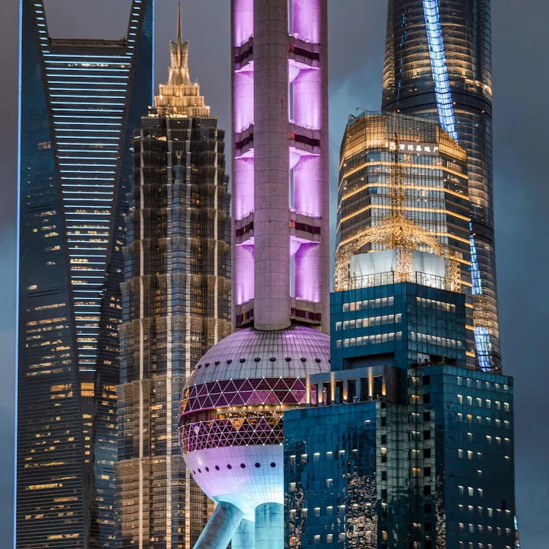 Close-up view of illuminated modern skyscrapers in a city skyline at dusk, including the Oriental Pearl Tower with purple lighting.