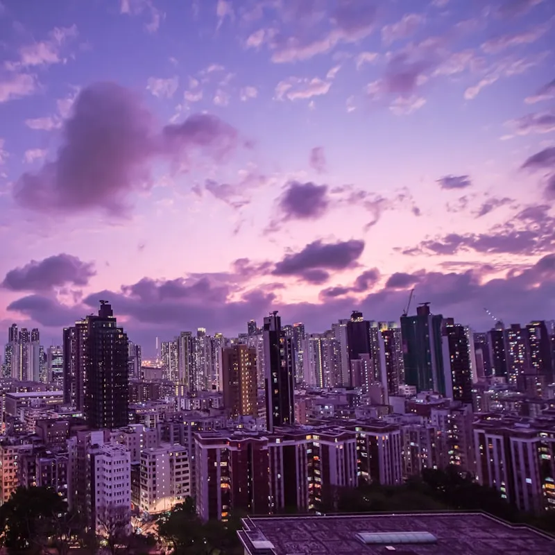 City skyline at dusk with high-rise buildings under a purple and pink cloudy sky.
