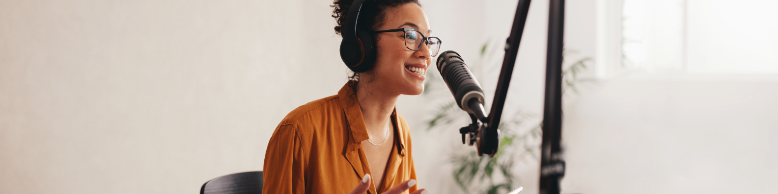 Smiling podcaster in orange shirt wearing headphones speaking into microphone