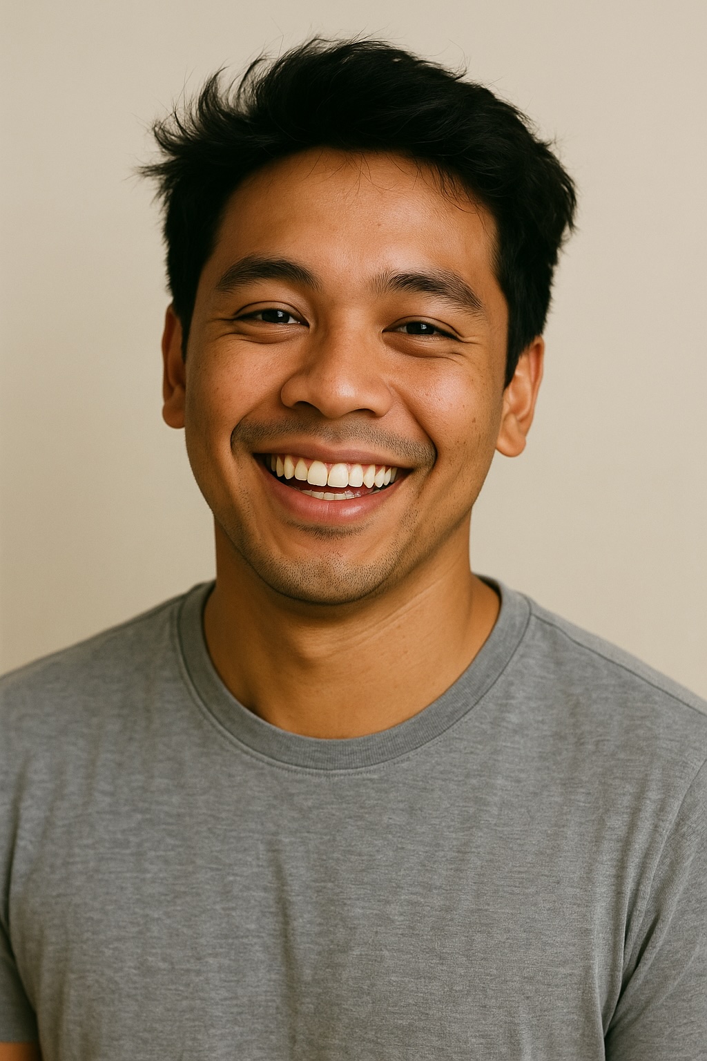 Young man in gray shirt smiling brightly against neutral background