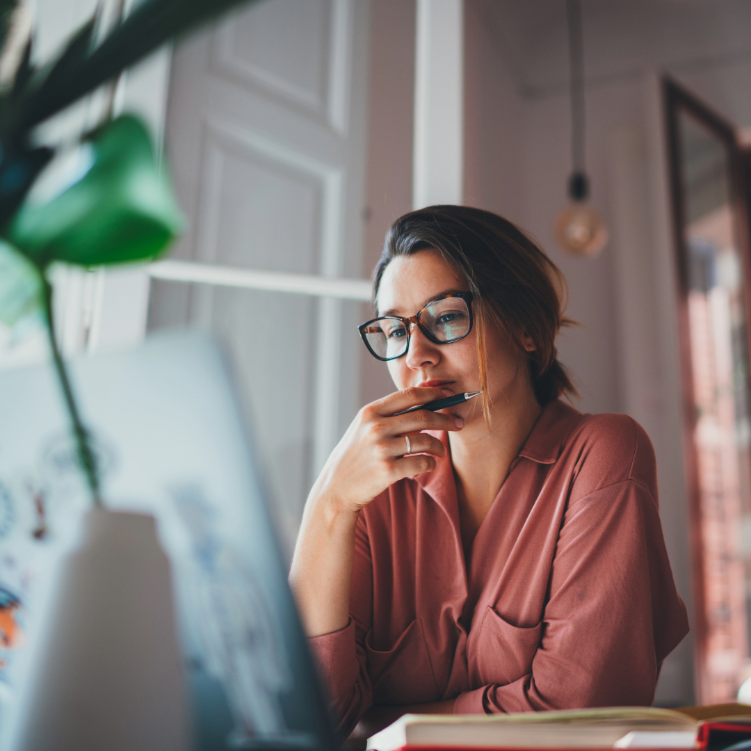 Woman in glasses thinking while working on laptop at home