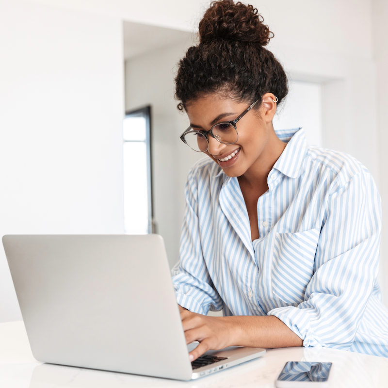 Smiling woman with curly hair and glasses working on laptop at home