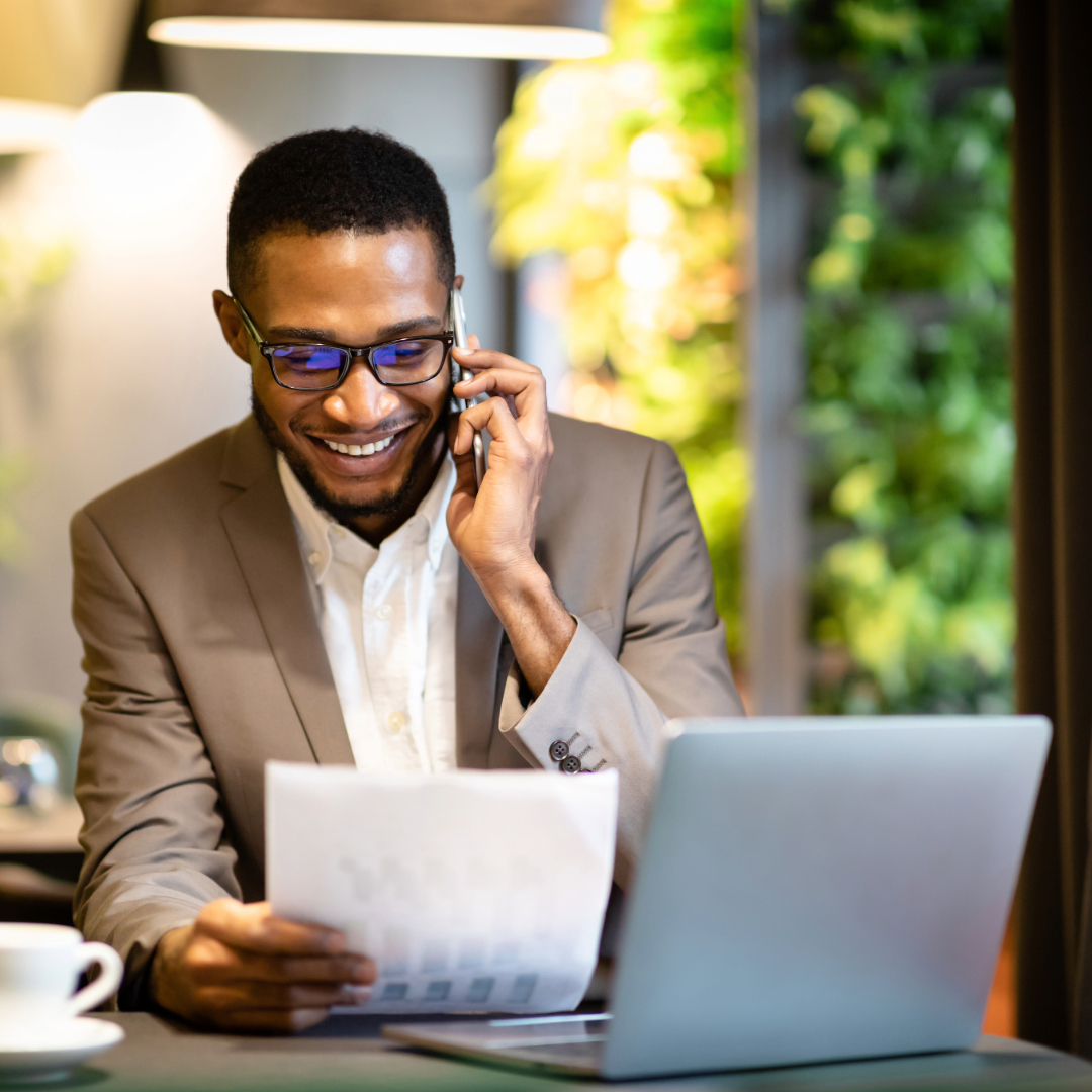 Smiling professional talking on phone while working on laptop and document