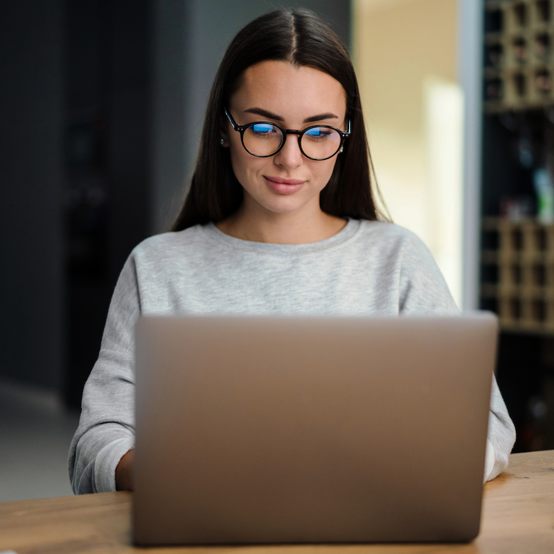 Person with glasses working on laptop at wooden desk