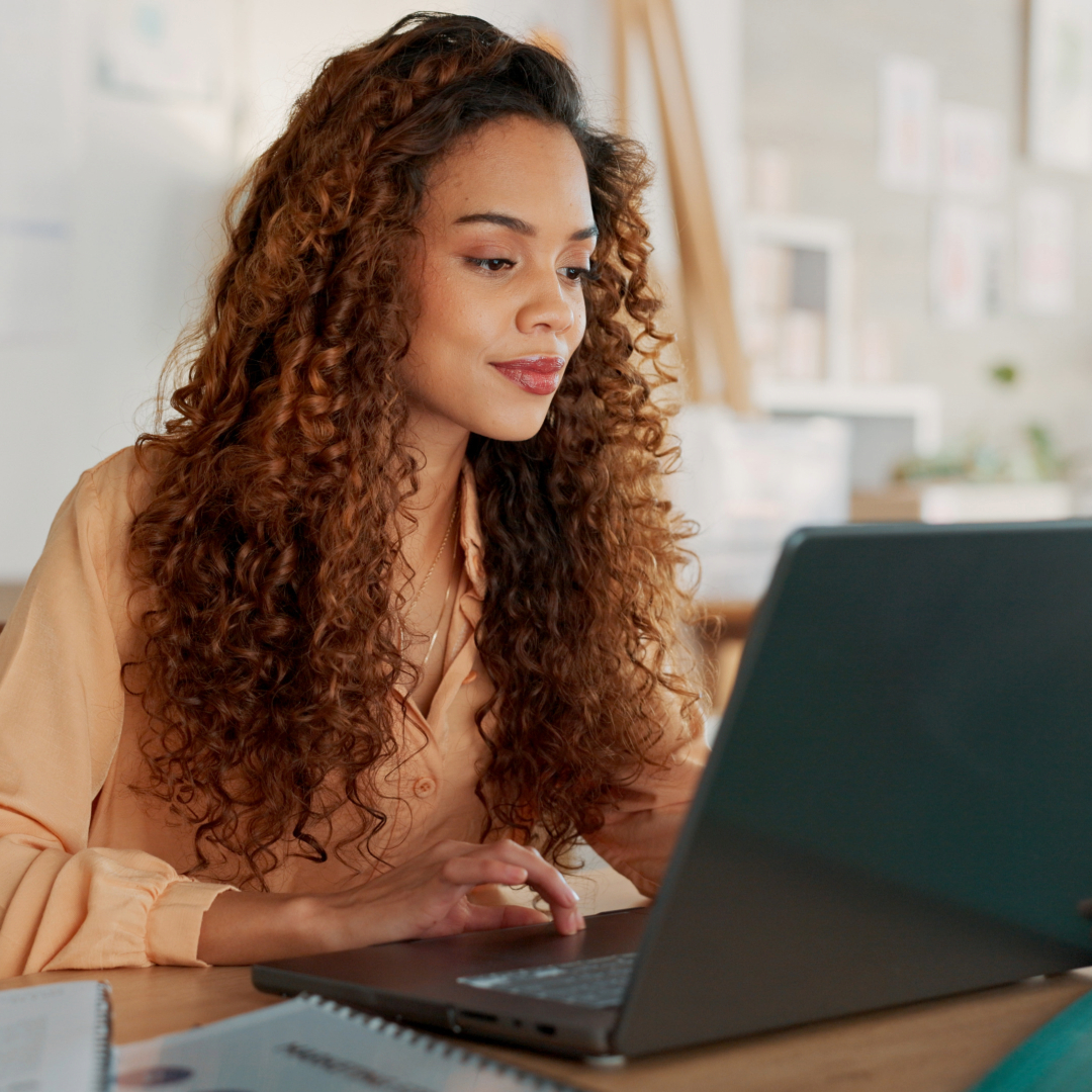 Woman with curly hair working on laptop in bright, modern office