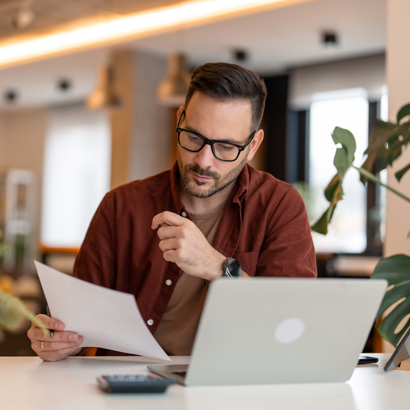 Professional working at laptop, reviewing document in modern office space