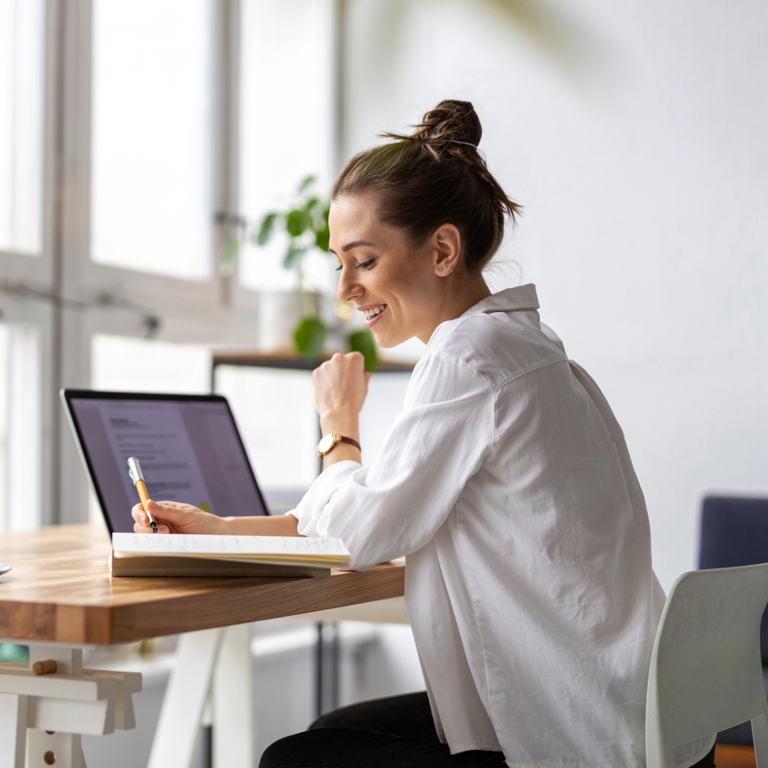 Smiling woman working on laptop at modern wooden desk near window