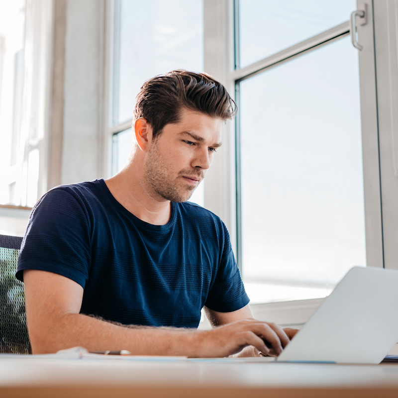 Person in blue shirt working on laptop by bright window