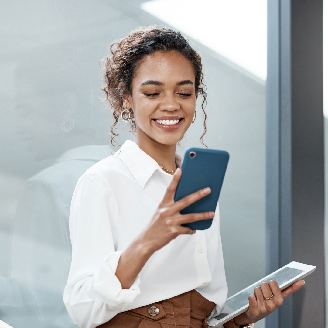 Smiling professional using smartphone and tablet near office window