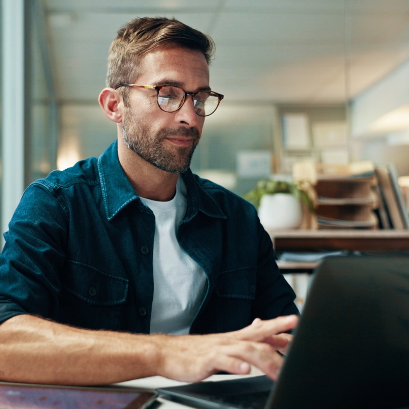 Professional working on laptop in modern office with glasses and blue shirt