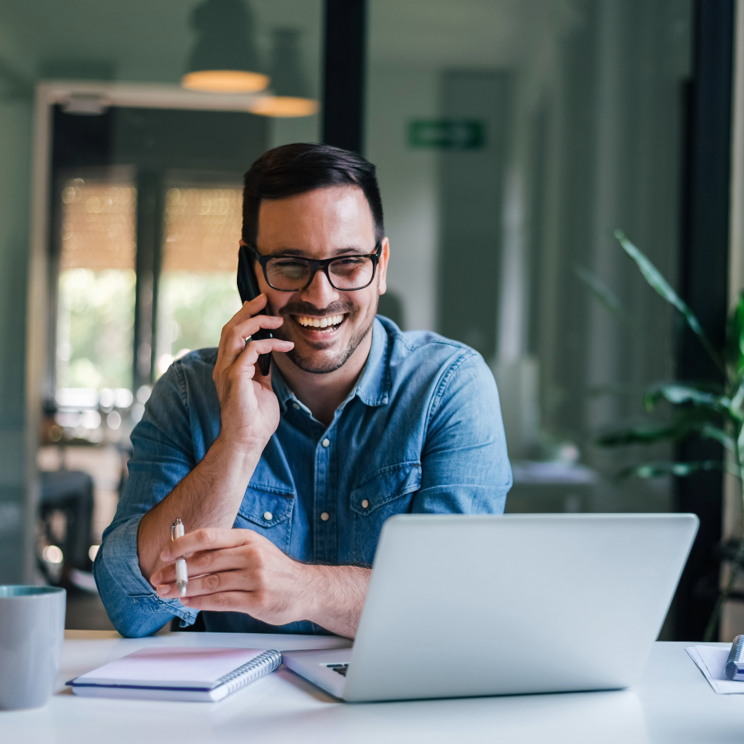 Smiling professional talking on phone while working on laptop in office