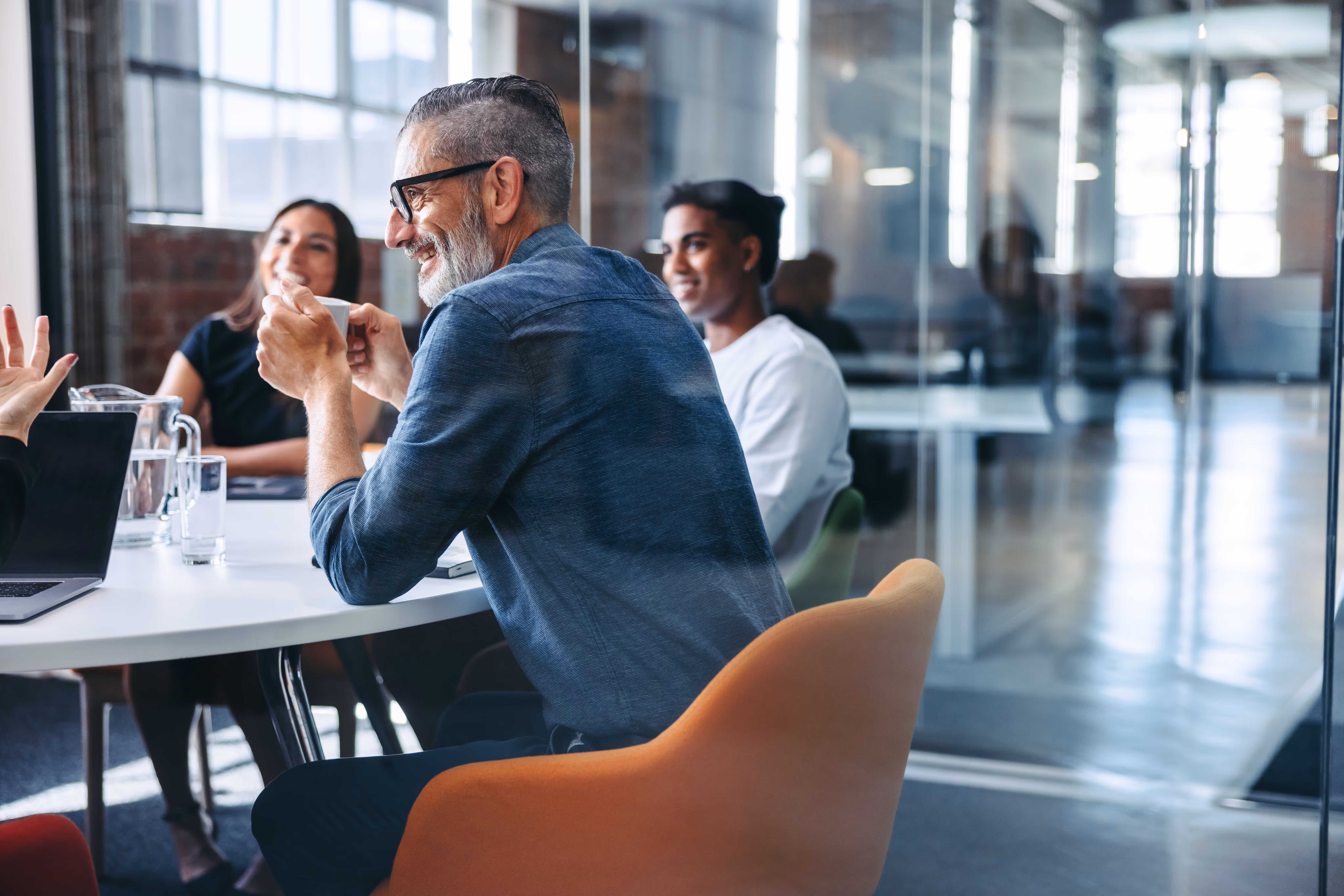 Smiling diverse colleagues having a discussion around a table in a modern office meeting room.