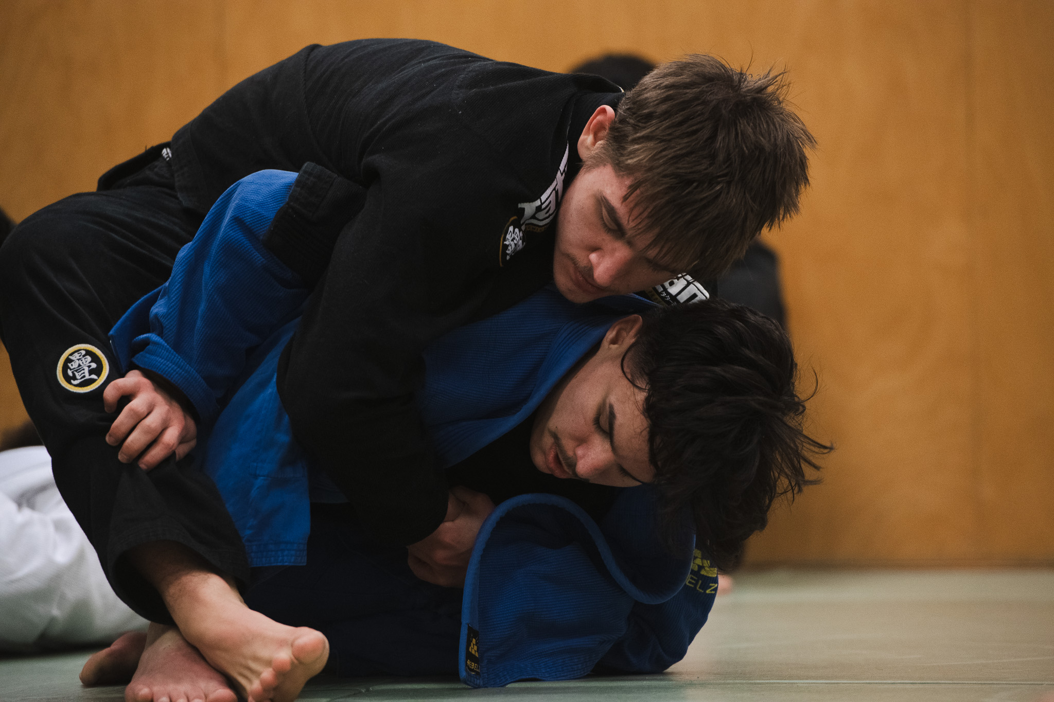 Two men engaged in Brazilian jiu-jitsu grappling on a mat, wearing black and blue gis.