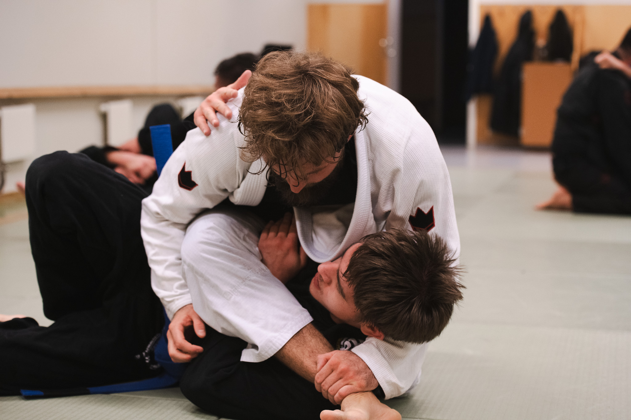 Two men practicing Brazilian Jiu-Jitsu grappling on a mat inside a dojo.